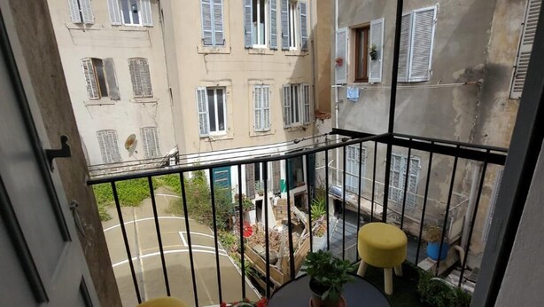 A small balcony with a round table and two yellow stools, surrounded by a metal railing. - Maison Pour Vacances (Marseille)