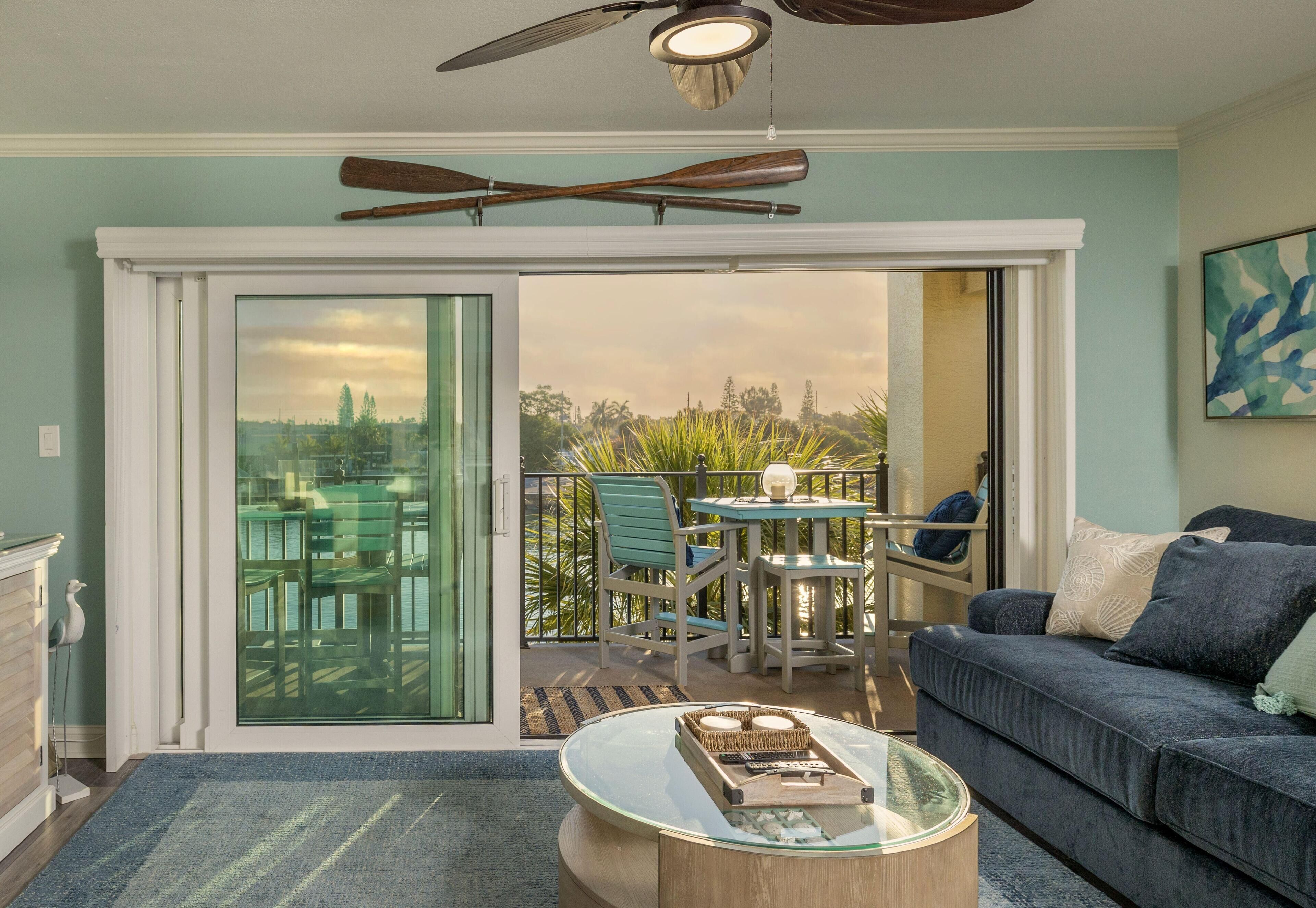 A living room with a glass sliding door leading to a balcony with outdoor furniture and a view of trees.