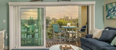 A living room with a glass sliding door leading to a balcony with outdoor furniture and a view of trees.