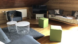 A cozy loft-style room with a wooden ceiling, a sofa, a TV, and a small decorative tree.