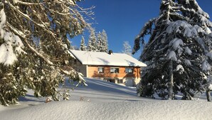 A snow-covered landscape with a wooden cabin and snow-laden trees.