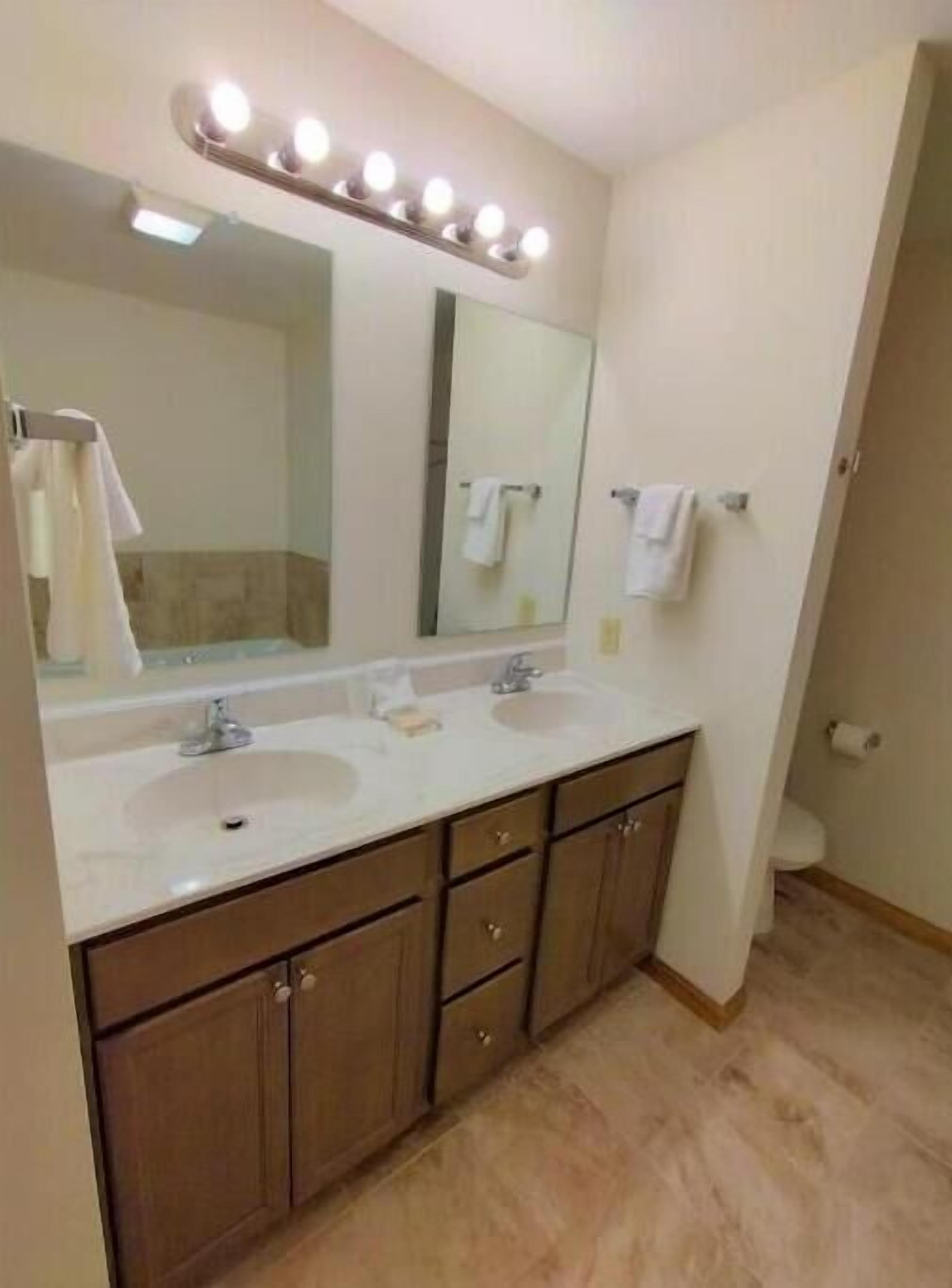 Un baño con dos lavamanos, un espejo grande e iluminación en el techo.