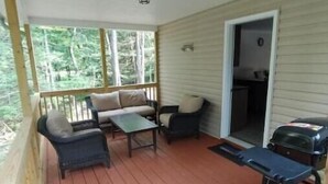 A covered porch with a wooden deck, a sofa, a small table, and a grill. - Spacious 3-bedroom house in the Poconos. (Blakeslee)
