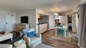 Un salon moderne comprenant un canapé, une table basse et un téléviseur. Il y a également un coin cuisine avec des placards et une table à manger avec des chaises.