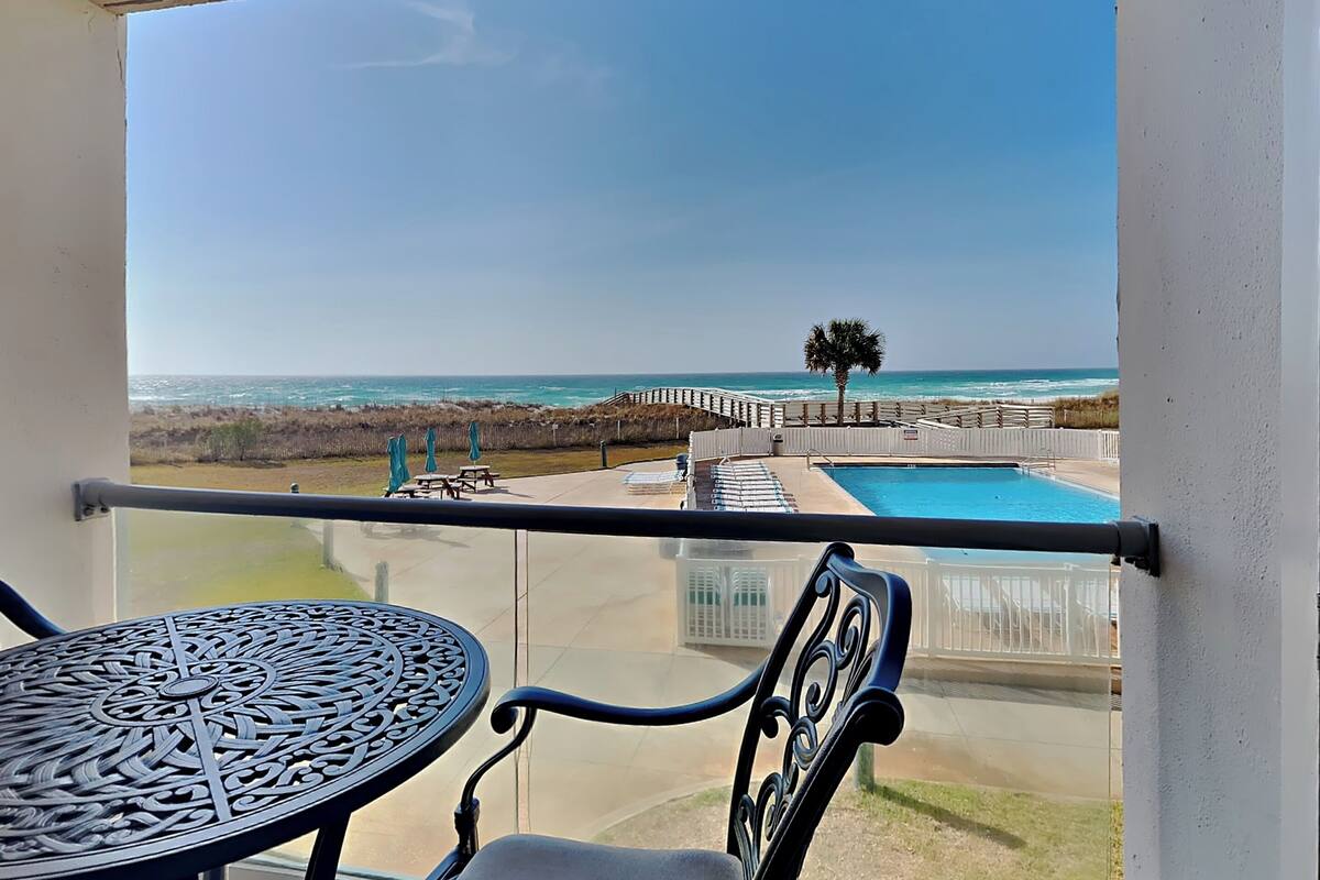 A balcony with a view of the ocean, a pool, and a palm tree.