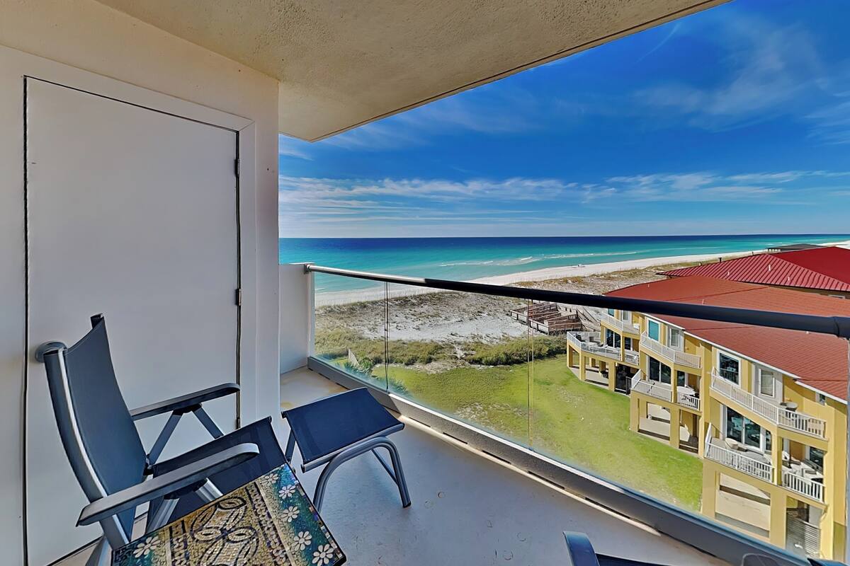 A balcony with a view of a beach and a building with a red roof.
