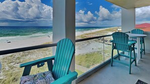 Un balcon avec des chaises turquoise et une table donnant sur une plage, sous un ciel dégagé.