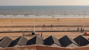 A beach with people walking, a no parking sign, and a row of buildings with sloped roofs. - Apt 8 @ Hunter's Quay (Bridlington)