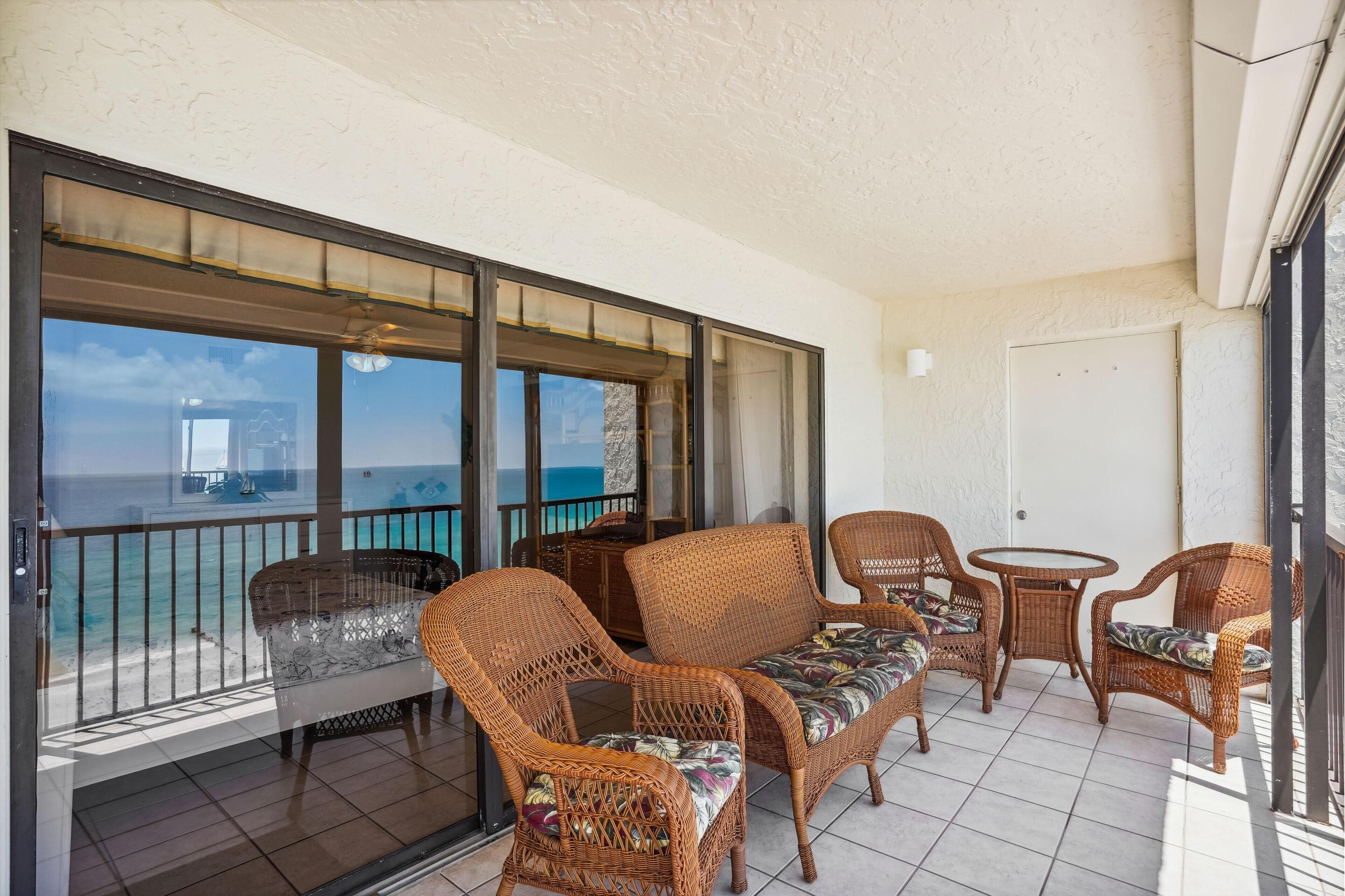 Een balkon met rieten meubels, uitzicht op zee en een plafondventilator.