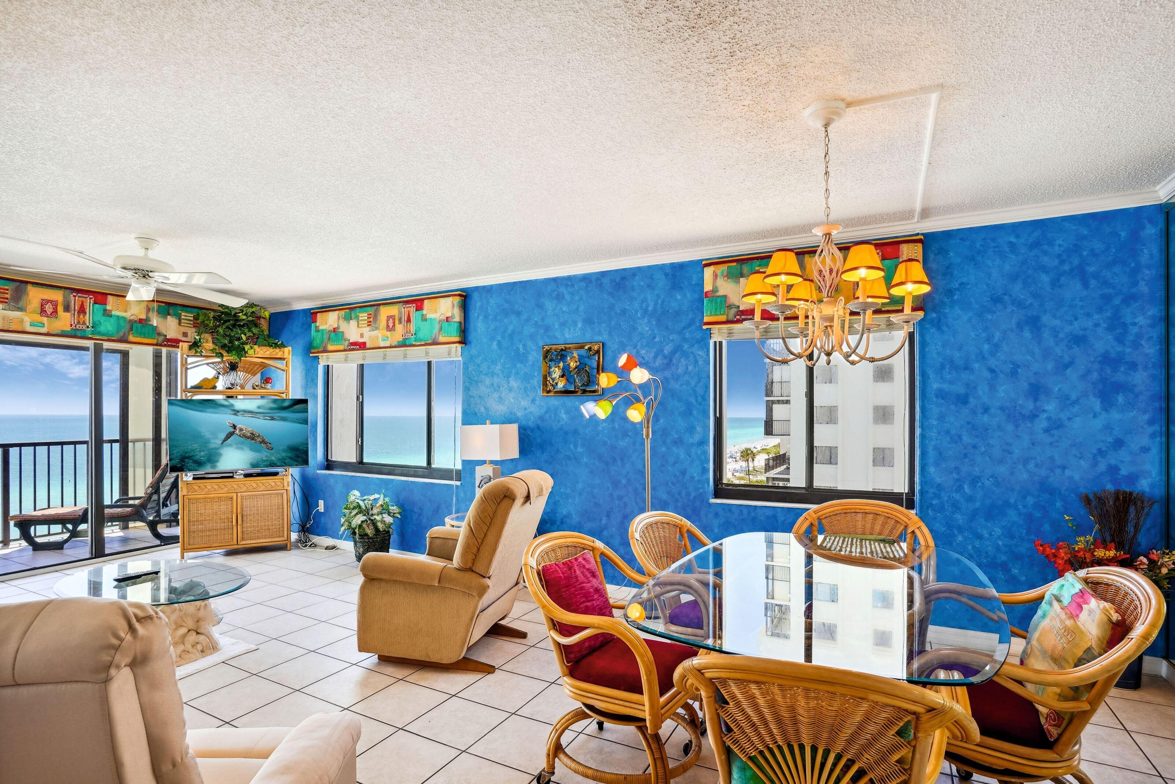 A living room with a television, wicker furniture, a chandelier, and a view of the ocean.