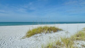 A sandy beach with sparse grass and a clear blue sky.