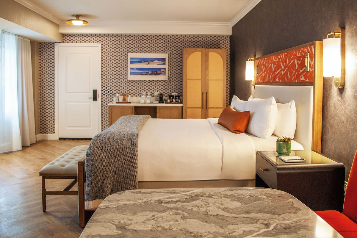 Une chambre d’hôtel comprenant un lit, une table de chevet, un banc et un bureau avec une chaise.