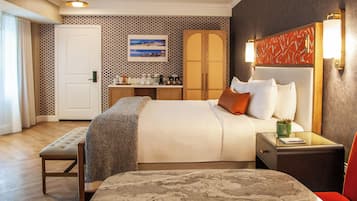 Habitación de hotel con cama, mesita de noche, banco y escritorio con silla.