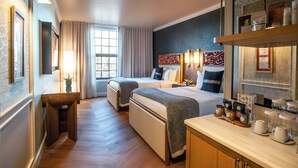 Une chambre d’hôtel avec deux lits, un petit bureau, une fenêtre avec des rideaux et un minibar contenant divers articles.