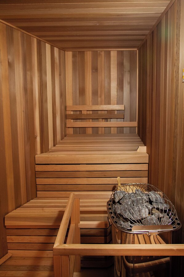 A wooden sauna with benches and a metal container for rocks.