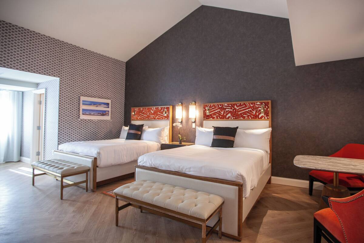 Une chambre d’hôtel moderne avec deux lits, un banc, une table et une chaise rouge.