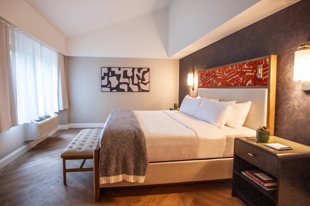 Une chambre d’hôtel moderne avec un grand lit, une banquette, une table de chevet et une œuvre d’art murale.