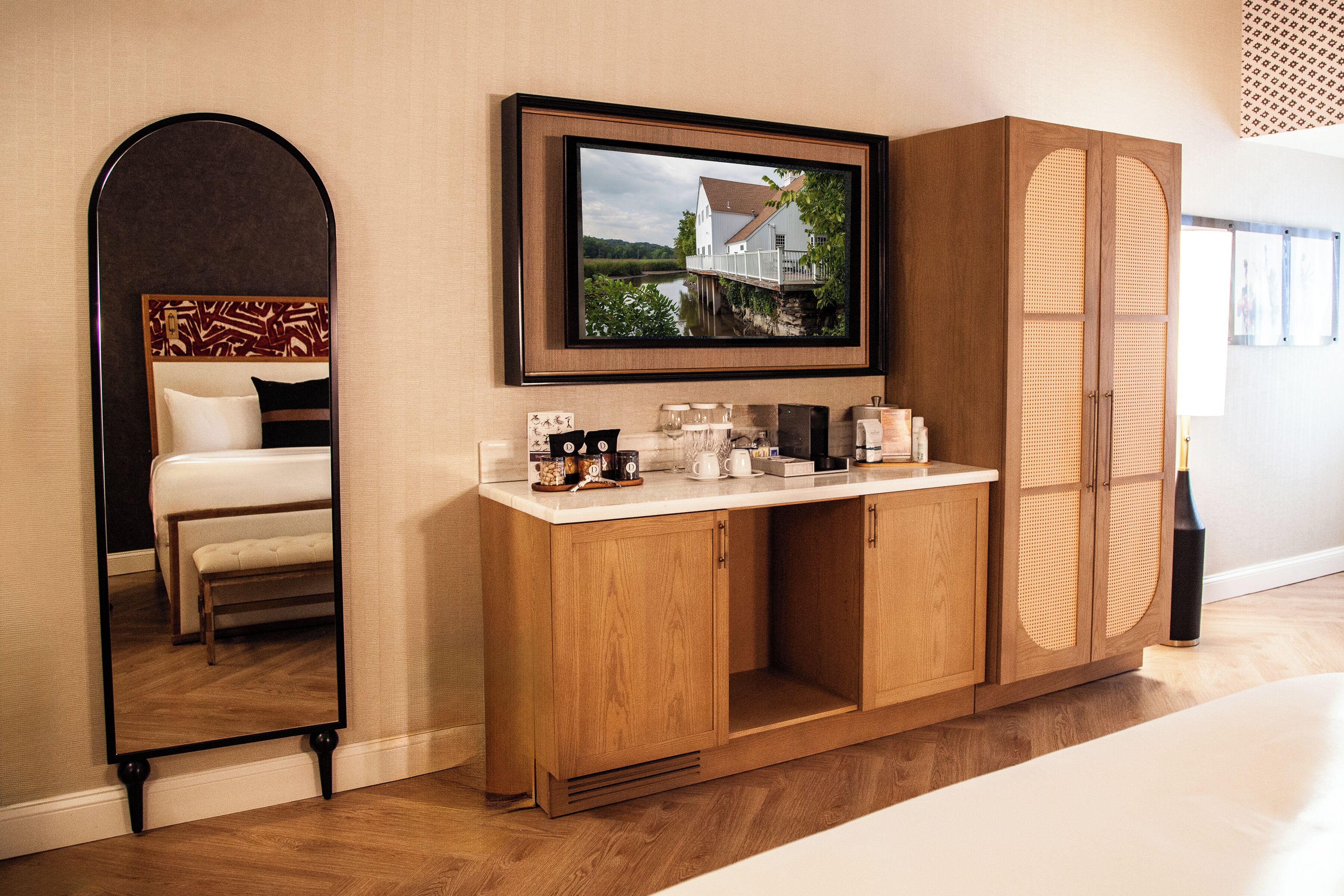A hotel room with a large mirror, a television mounted above a wooden cabinet, and a bed with a headboard.