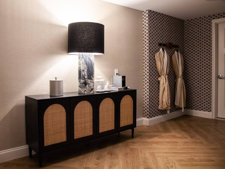 A corner room with a dark wood console table, a marble lamp, and patterned wallpaper.