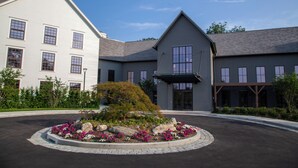 Un bâtiment à la façade blanche et au toit gris, entouré d’un jardin aménagé avec des rochers et des fleurs.