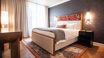 A modern hotel room with a large bed, a nightstand, a desk, and a patterned rug.