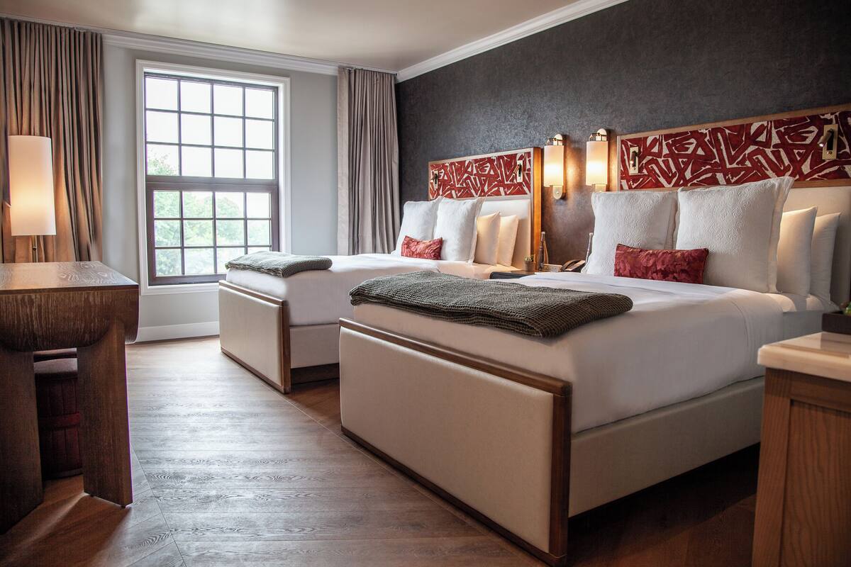 Une chambre d’hôtel avec deux lits, un bureau et une grande fenêtre avec des rideaux.