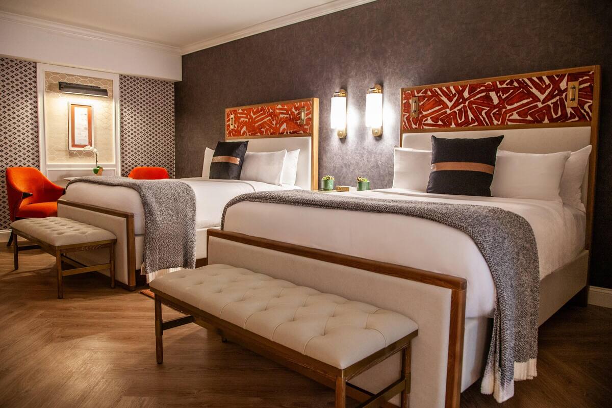 Une chambre d’hôtel avec deux lits, un banc et une chaise.