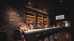 Un bar avec un mur en pierre, de nombreuses étagères remplies de bouteilles et des tabourets de bar.