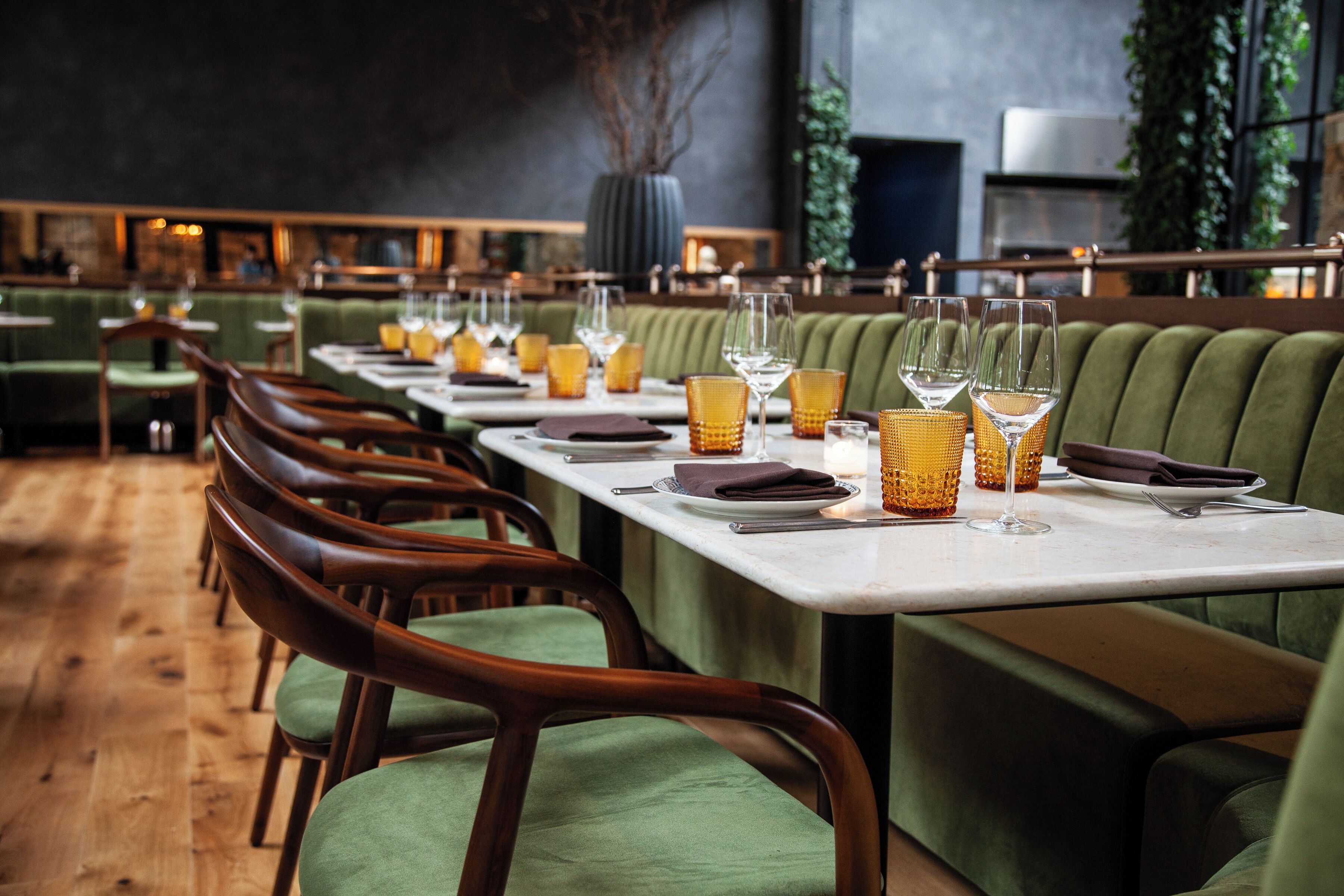 A restaurant with green upholstered booths and wooden chairs, arranged in a long dining area with white tables set for service.