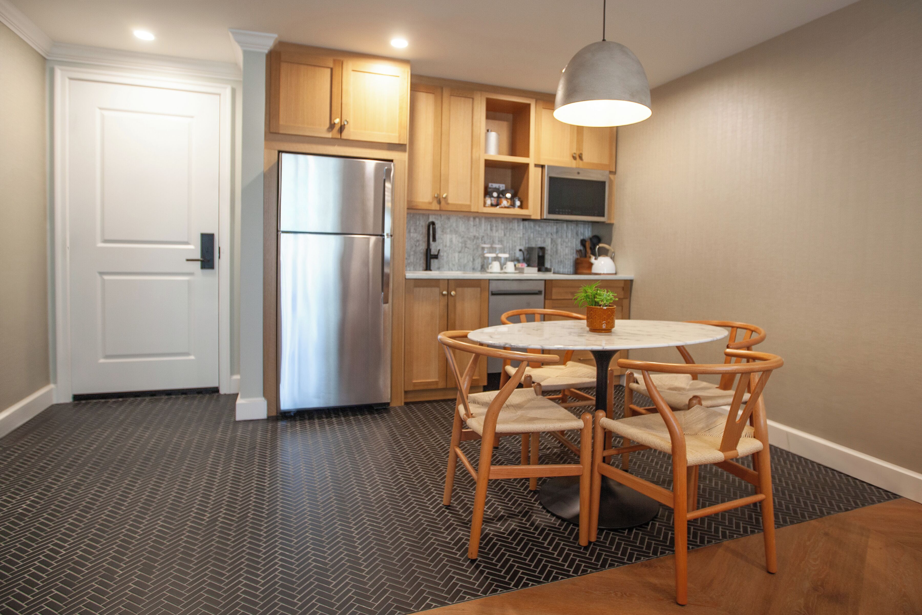 A compact kitchen with wooden cabinets, a stainless steel refrigerator, a microwave, and a round table with chairs.