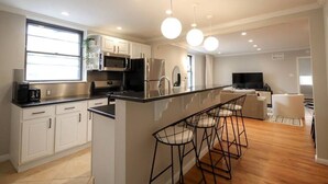 Una cocina moderna con gabinetes blancos, encimera negra y una isla central con taburetes de bar.