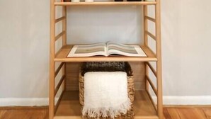 Una estantería de madera con tres repisas, un florero blanco y un libro.