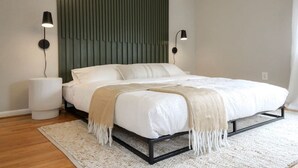 Un dormitorio moderno con una cama, dos lámparas de noche, una alfombra texturizada y un panel en la pared.