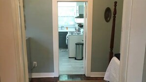A hallway leading to a kitchen with a stove, sink, and trash can. - The Alexandria House #1 (Jackson)