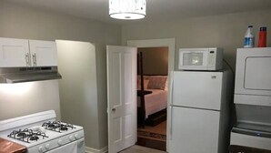 A compact kitchen with a gas stove, oven, microwave, and refrigerator. A dining table with chairs is in the foreground. - The Alexandria House #1 (Jackson)