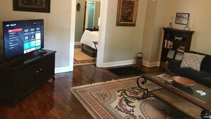 A living room with a flat-screen TV, a dark-colored sofa, a coffee table, and a patterned rug. - The Alexandria House #1 (Jackson)
