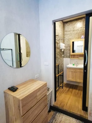 A modern bathroom with a wooden vanity, a round mirror, and a stone-textured wall.