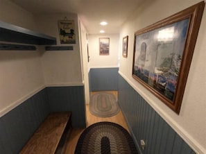 A narrow hallway with a bench, a rug, and a framed picture on the wall.