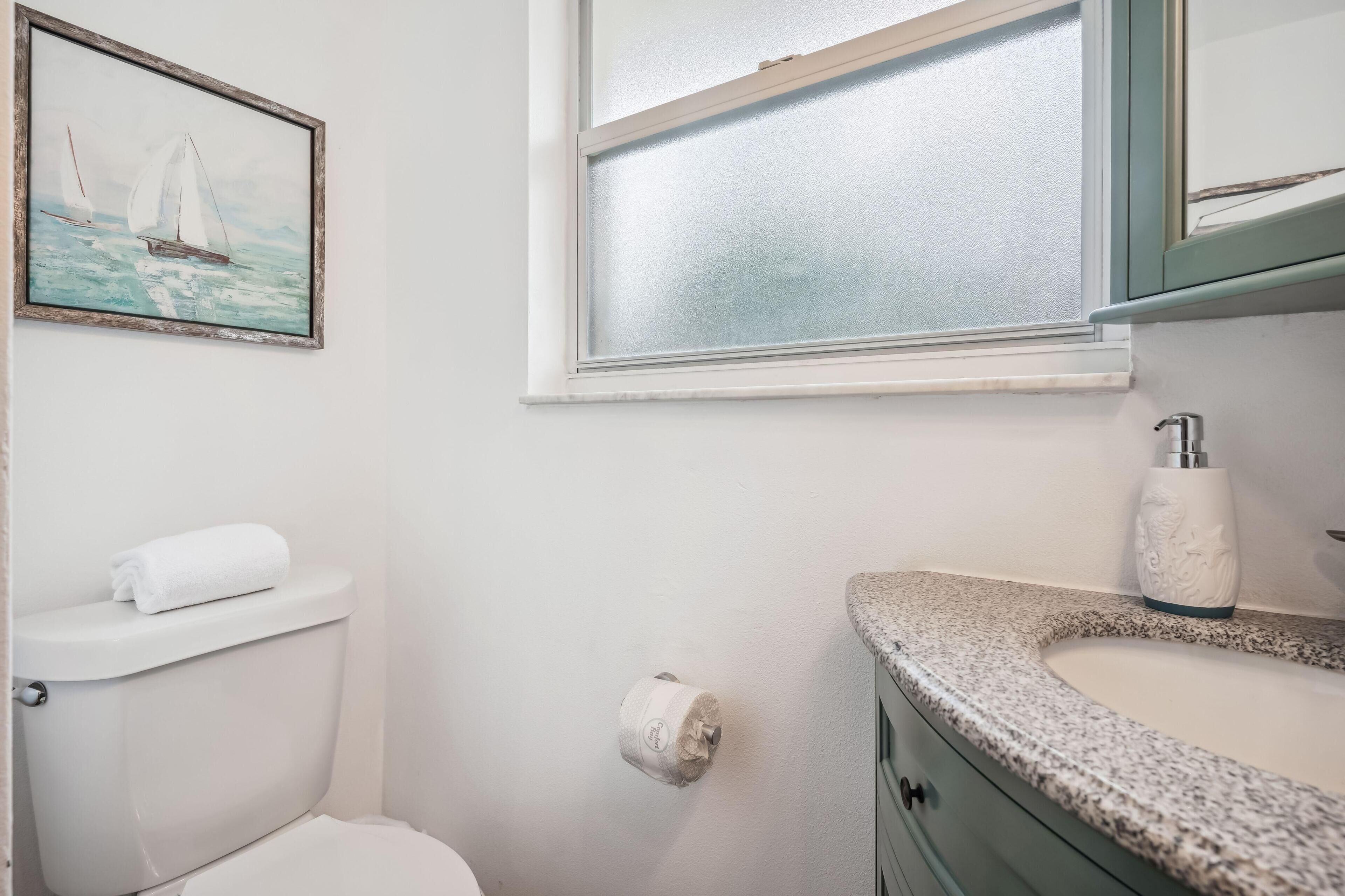 Ein Badezimmer mit Toilette, Waschbecken, einem Bilderrahmen mit Segelbooten und einem Fenster.