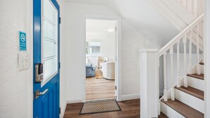A hallway with a blue door, white walls, a wooden floor, and a white staircase. - Beach Livin 1 - 1 Bedroom Downstairs (Treasure Island)