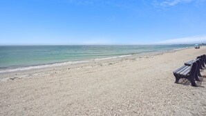 A beach with pebbly sand and a row of wooden benches along the shore. - Beach Livin 1 - 1 Bedroom Downstairs (Treasure Island)