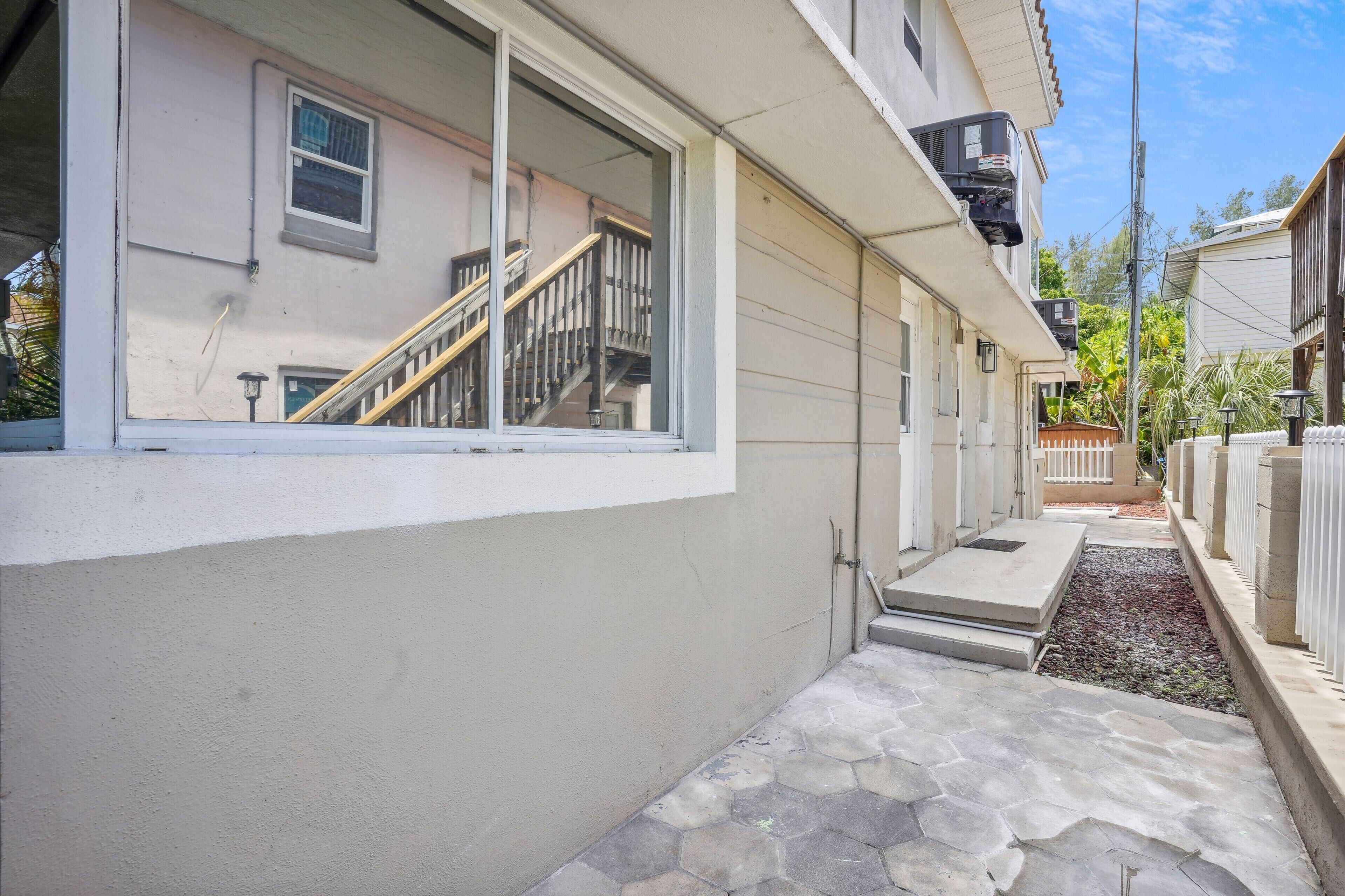 A residential building with a stone pathway, a wooden staircase, and a window with a view of a staircase leading to a balcony.