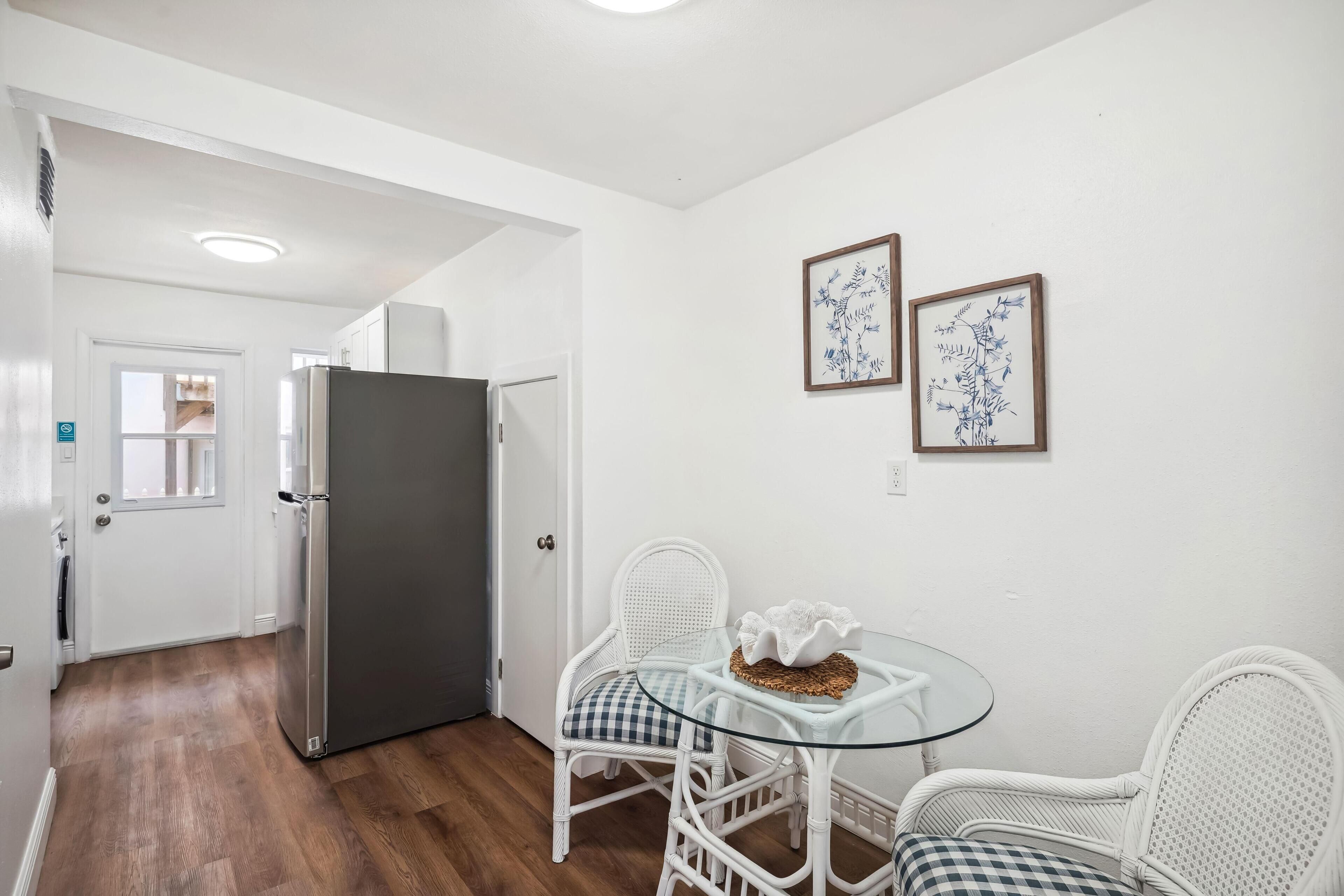 A compact kitchen with a refrigerator, a dining table with chairs, and two framed wall art pieces.