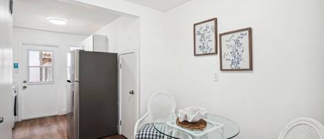 A compact kitchen with a refrigerator, a dining table with chairs, and two framed wall art pieces.