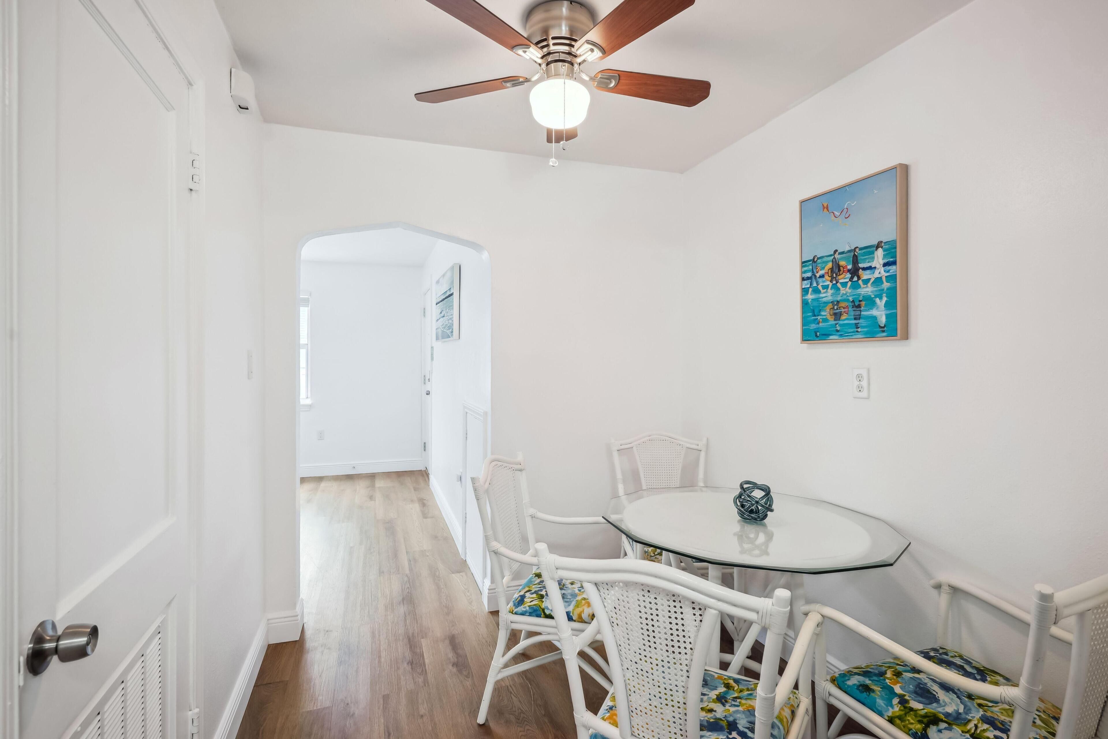 A dining area with a round glass table, white wicker chairs, and a ceiling fan.