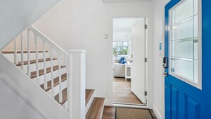 A staircase leading to a second floor, a blue door with a glass panel, and a view into a living area with a white couch and a small table. - Beach Livin 2 - 1 Bedroom Downstairs (Treasure Island)