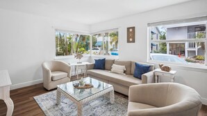 A modern living room with a beige sofa, a glass coffee table, and a white side table. - Beach Livin - All (Treasure Island)