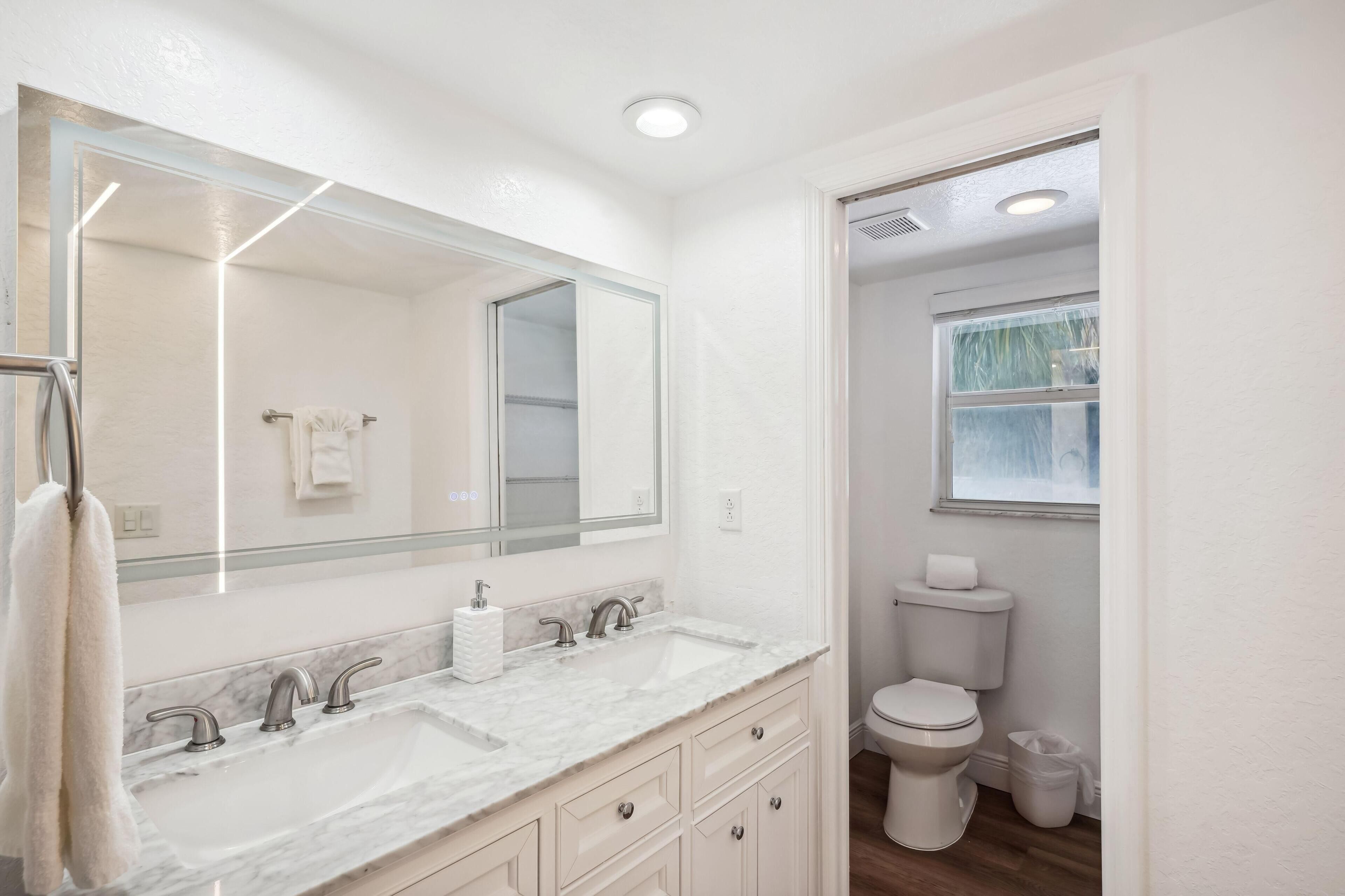 Een moderne badkamer met een grote spiegel, twee wastafels en een toilet.