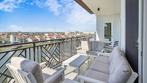 A balcony with a sofa, chairs, and a table overlooking a marina and buildings.