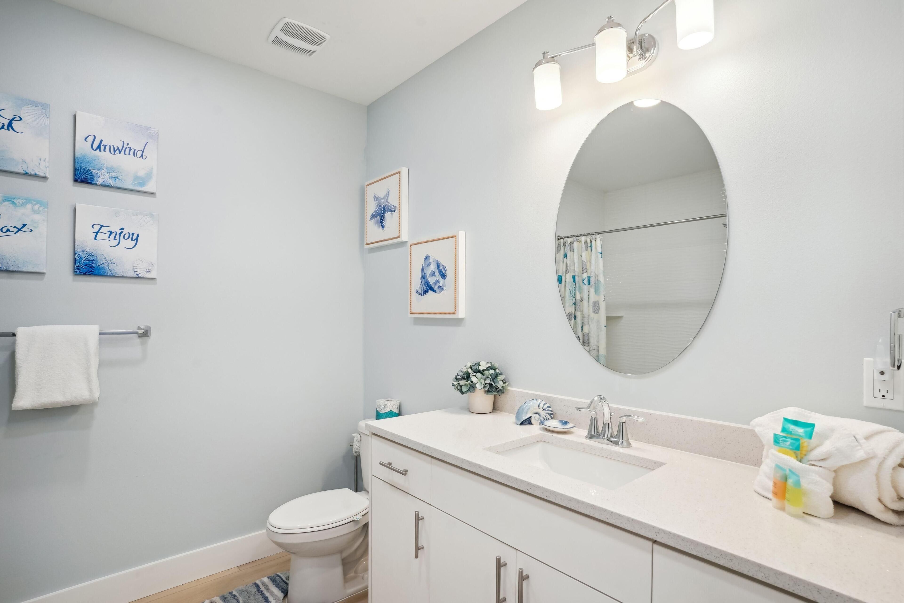 A bathroom with a white sink, vanity, and a large mirror. There are framed pictures on the wall and a towel rack with a white towel.
